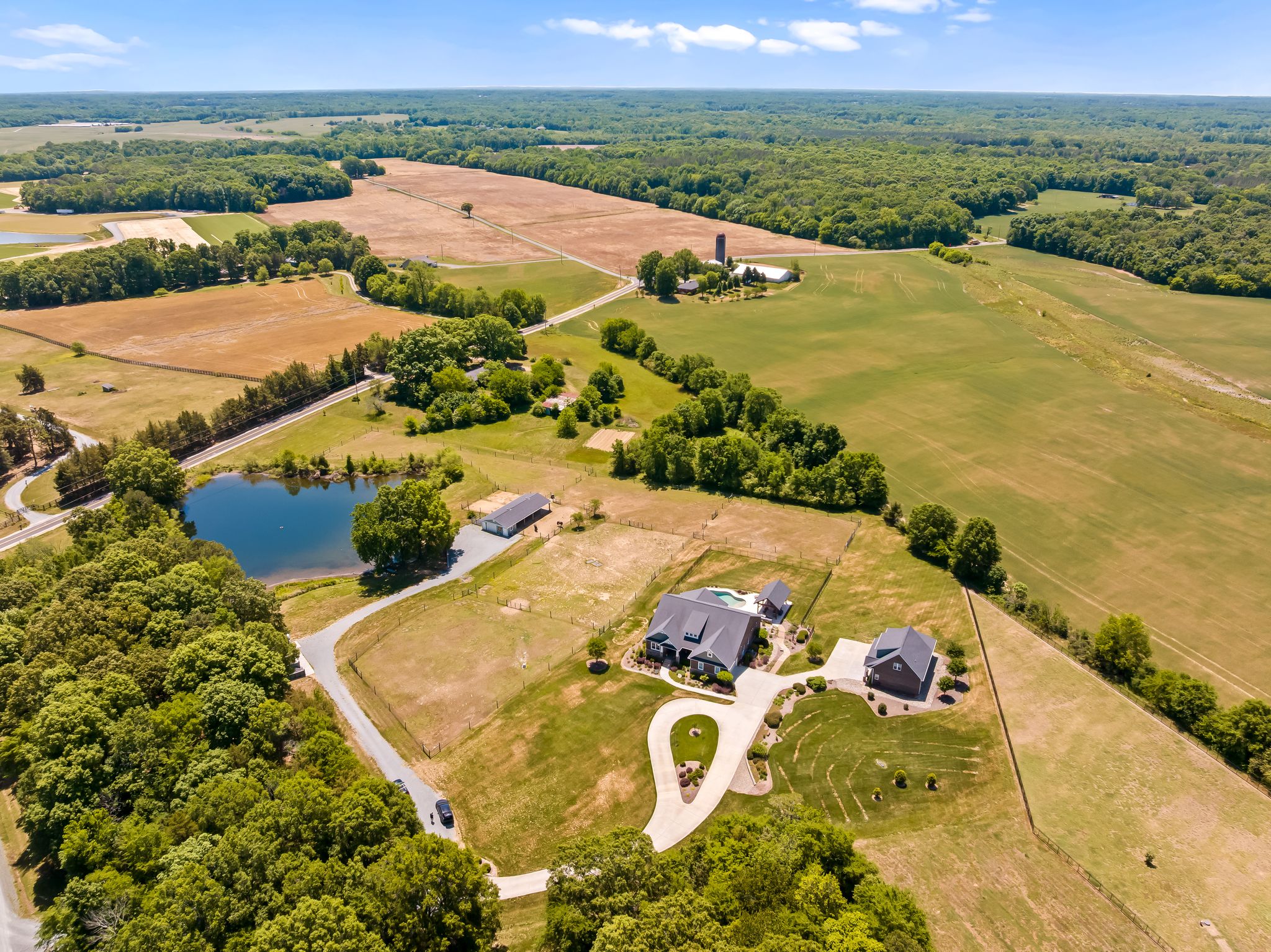 Wide aerial showing the home, pond, barn, and pastures
